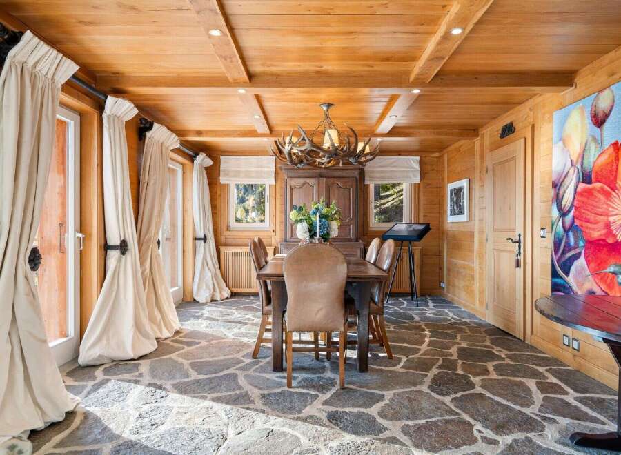 This stunning dining room boasts a rustic-chic design with a wood-paneled ceiling, stone flooring, and large windows that let in plenty of natural light.