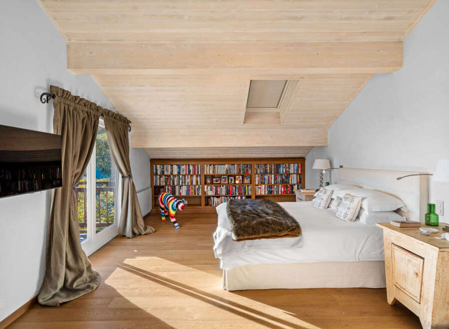 This luxurious bedroom boasts a stunning wooden ceiling, large windows offering scenic views, and ample built-in bookshelves.