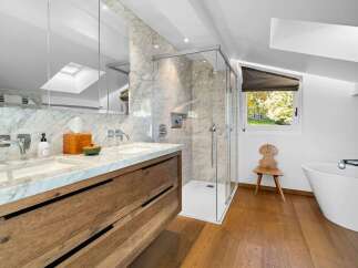 Luxurious bathroom with marble finishes and wooden vanity, featuring a spacious shower and a freestanding bathtub.
