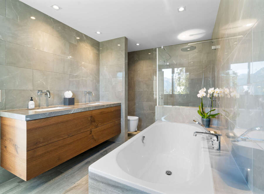 This luxurious bathroom boasts a spacious freestanding bathtub, a double vanity with wooden cabinetry, and a walk-in shower enclosed in glass.