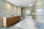 This luxurious bathroom boasts a spacious freestanding bathtub, a double vanity with wooden cabinetry, and a walk-in shower enclosed in glass.