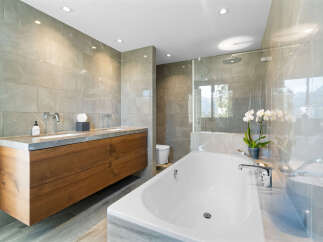 This luxurious bathroom boasts a spacious freestanding bathtub, a double vanity with wooden cabinetry, and a walk-in shower enclosed in glass.