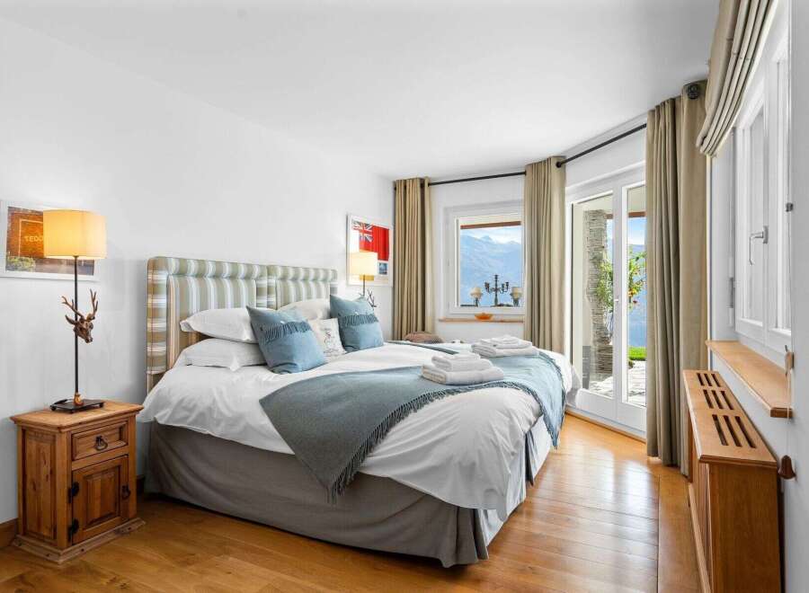 This luxurious bedroom boasts stunning lake views from its large windows and patio doors.