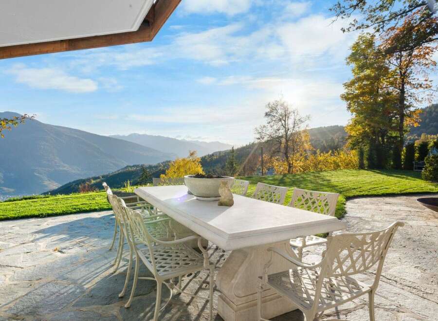 Luxury mountain retreat with expansive patio featuring a large stone table and ornate chairs, perfect for al fresco dining while enjoying breathtaking views.