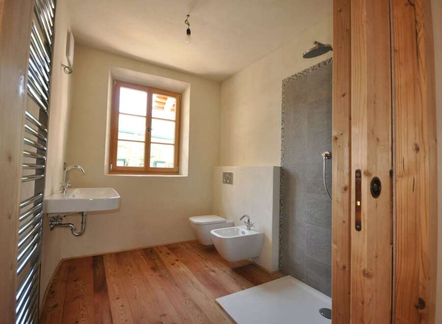 This charming bathroom features a rustic wooden floor and a bright window that fills the space with natural light.