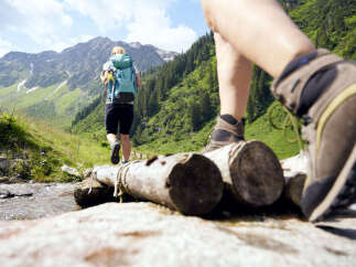Explore the beauty of nature with this stunning image of hikers crossing a wooden bridge.