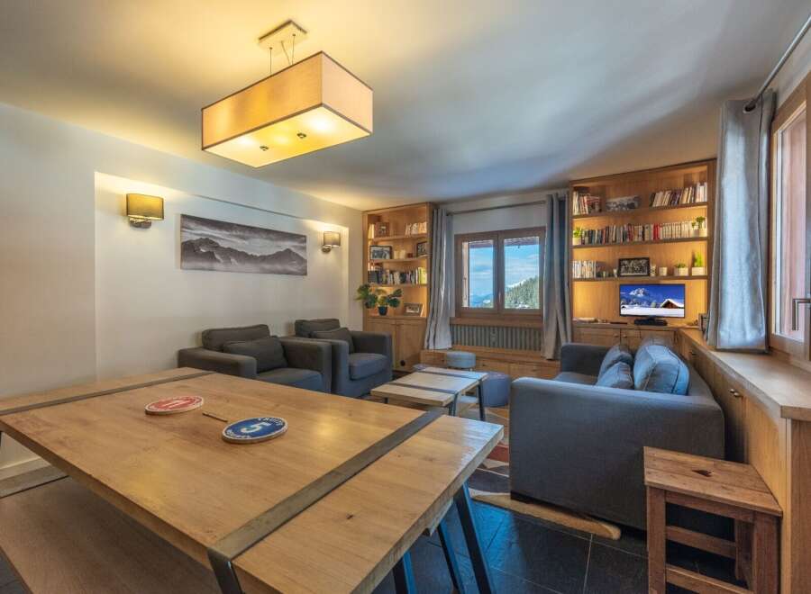 This stunning apartment boasts a spacious living area with comfortable seating, a large wooden dining table, and built-in bookshelves.