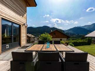Enjoy breathtaking mountain views from this stunning property's expansive wooden deck, perfect for al fresco dining.