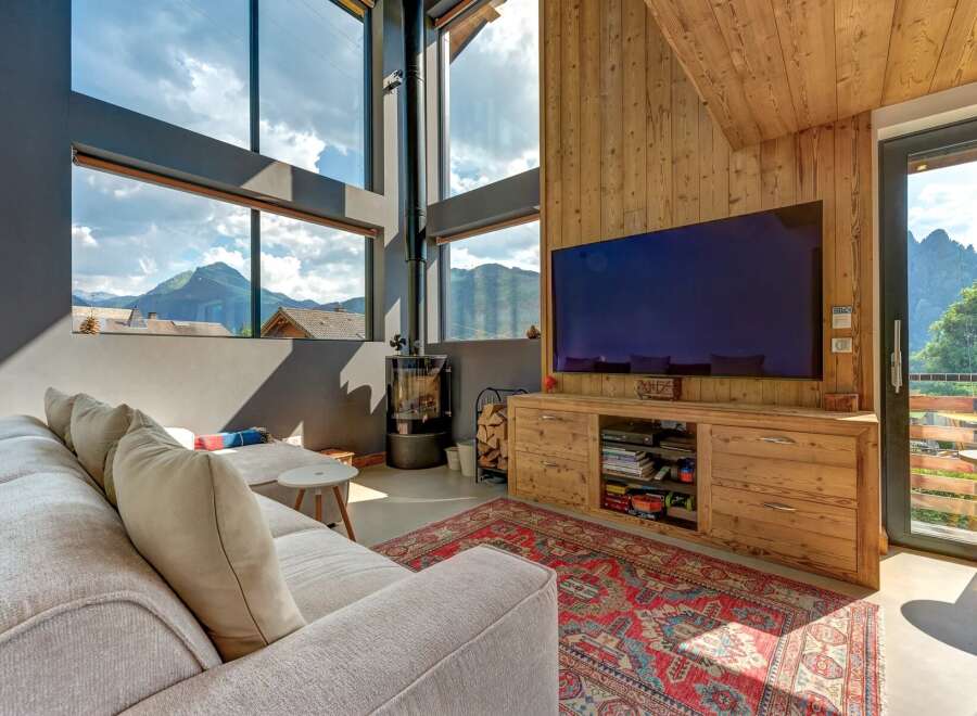 Experience breathtaking mountain views from this modern living room, featuring a large sectional sofa and a cozy wood-burning stove.