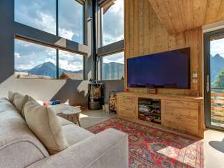 Experience breathtaking mountain views from this modern living room, featuring a large sectional sofa and a cozy wood-burning stove.