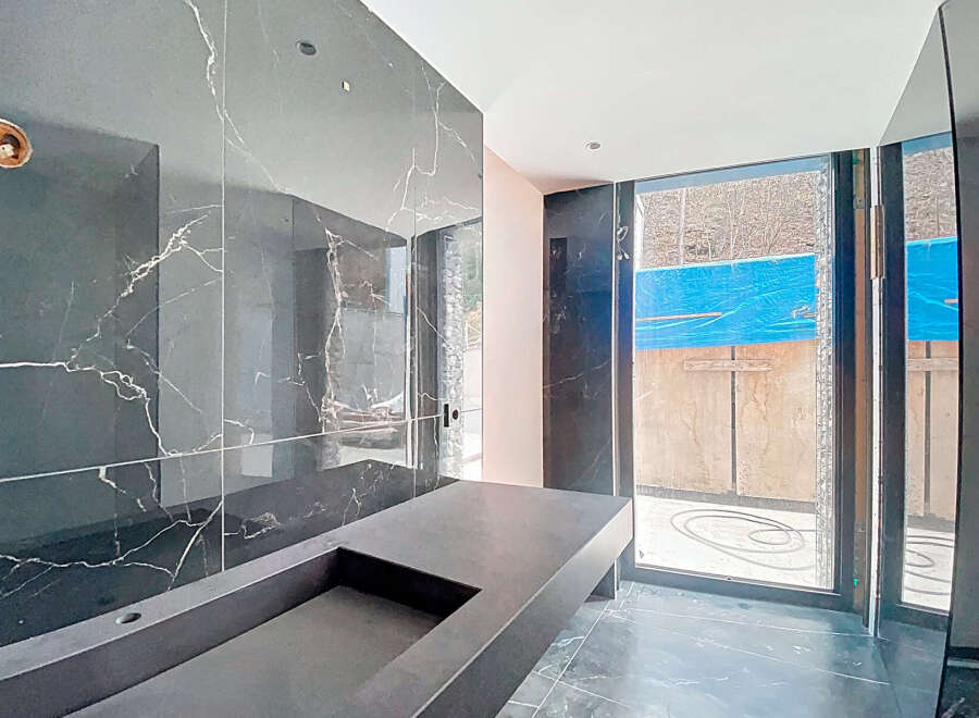 This stunning bathroom boasts a sleek, modern design with dark marble walls and a custom concrete sink.