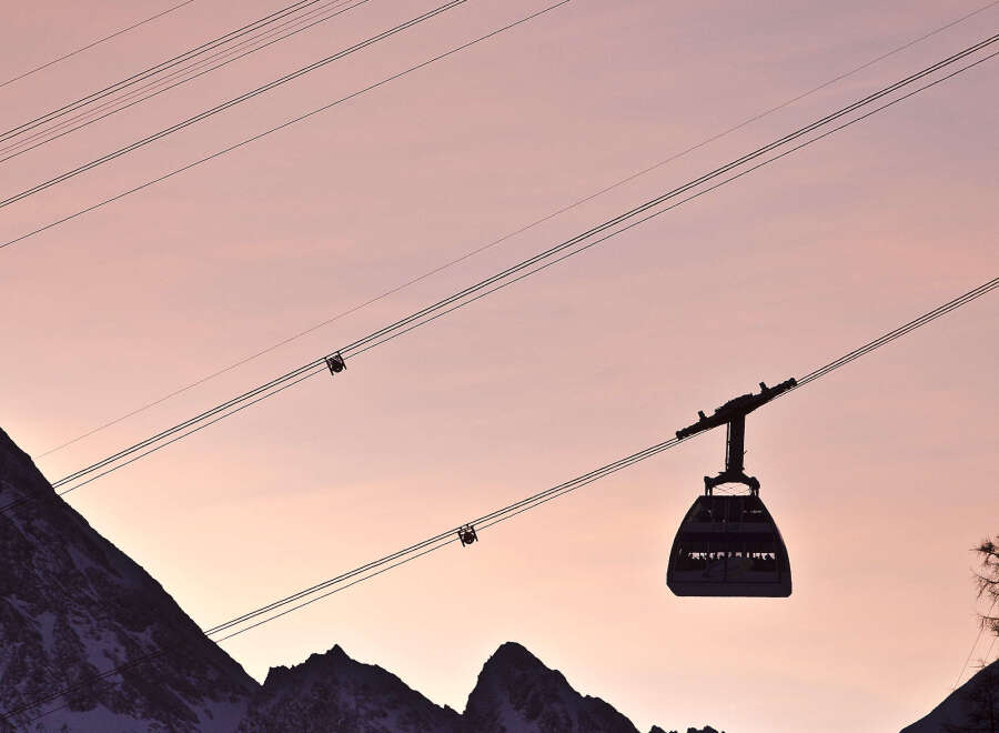 Silhouette of a cable car gliding against a breathtaking sunset backdrop, with snow-capped mountains creating a picturesque winter scene.