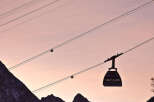 Silhouette of a cable car gliding against a breathtaking sunset backdrop, with snow-capped mountains creating a picturesque winter scene.