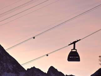Silhouette of a cable car gliding against a breathtaking sunset backdrop, with snow-capped mountains creating a picturesque winter scene.