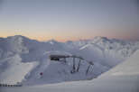 Sunrise paints the snow-capped Austrian Alps in soft pink hues, as seen from a ski lift station.