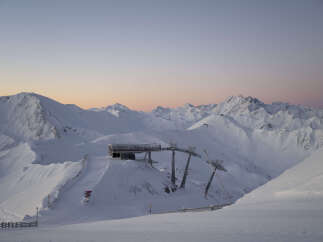 Sunrise paints the snow-capped Austrian Alps in soft pink hues, as seen from a ski lift station.