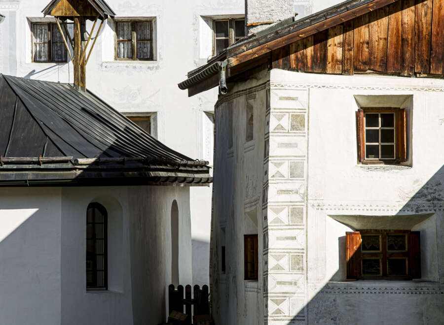 This charming European-style building features a mix of architectural elements, including a dark metal roof, wooden accents, and whitewashed walls adorned with decorative patterns.