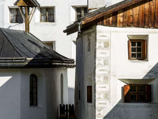 This charming European-style building features a mix of architectural elements, including a dark metal roof, wooden accents, and whitewashed walls adorned with decorative patterns.