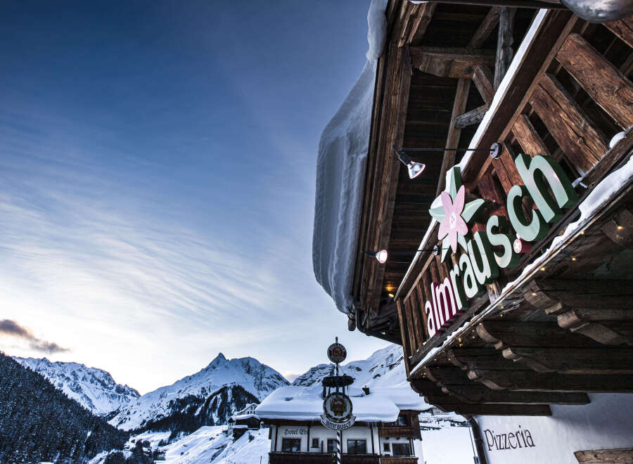 Nestled in a breathtaking snowy mountain setting, this charming pizzeria boasts a rustic wooden exterior with a unique overhanging design.