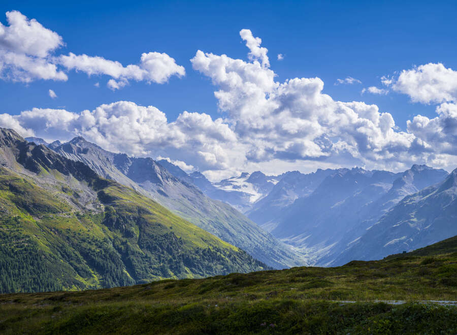 Majestic mountain range with a glacier visible in the distance, under a partly cloudy sky.