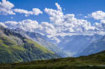 Majestic mountain range with a glacier visible in the distance, under a partly cloudy sky.