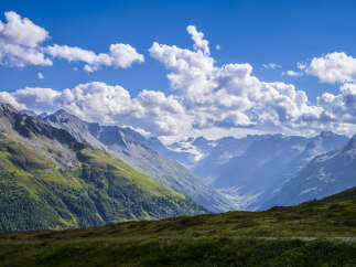 Majestic mountain range with a glacier visible in the distance, under a partly cloudy sky.