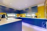 This modern kitchen boasts a sleek design with vibrant blue cabinetry and a contrasting white countertop.