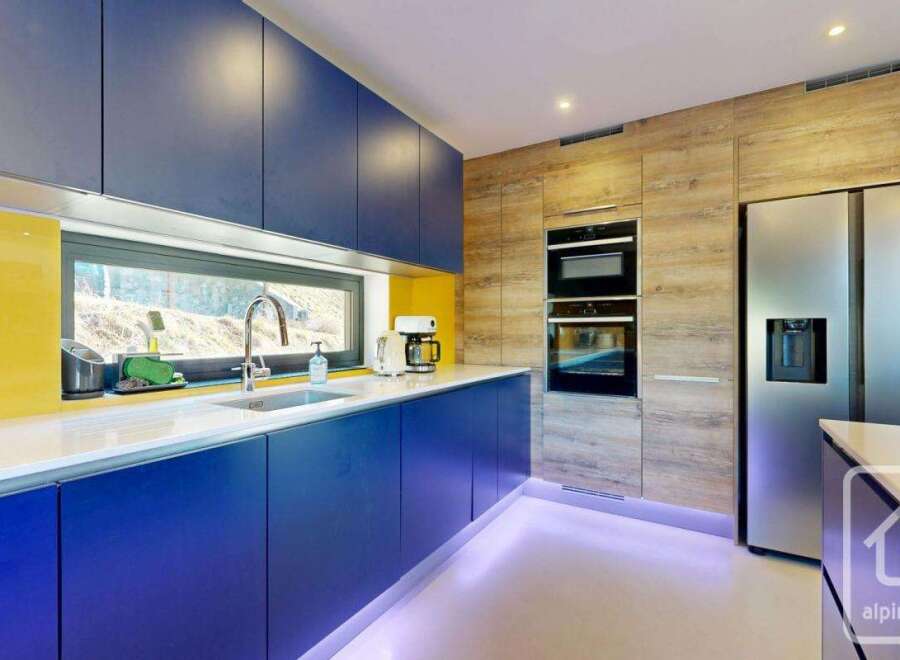 This modern kitchen boasts sleek, blue cabinetry and a bright yellow backsplash, creating a vibrant and stylish space.