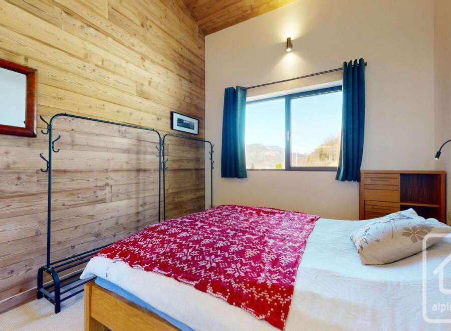 This cozy bedroom features a rustic wooden wall and a comfortable bed with a vibrant red blanket.