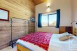 This cozy bedroom features a rustic wooden wall and a comfortable bed with a vibrant red blanket.