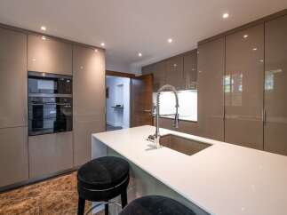 This stunning kitchen boasts sleek, modern cabinetry in a sophisticated taupe finish, complemented by a pristine white quartz countertop and a stylish chrome faucet.