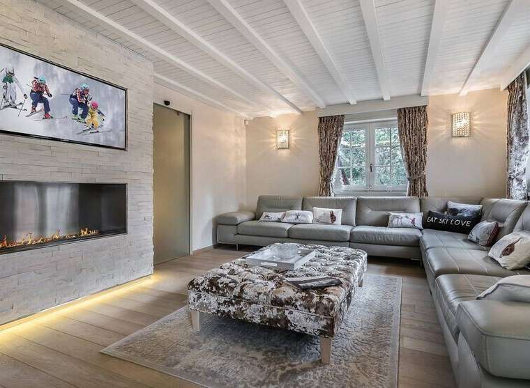 Luxurious chalet living room with a stunning stone fireplace, large sectional sofa, and a wall-mounted TV showcasing winter sports.