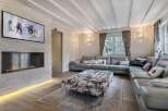 Luxurious chalet living room with a stunning stone fireplace, large sectional sofa, and a wall-mounted TV showcasing winter sports.