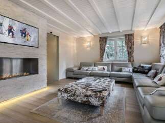 Luxurious chalet living room with a stunning stone fireplace, large sectional sofa, and a wall-mounted TV showcasing winter sports.