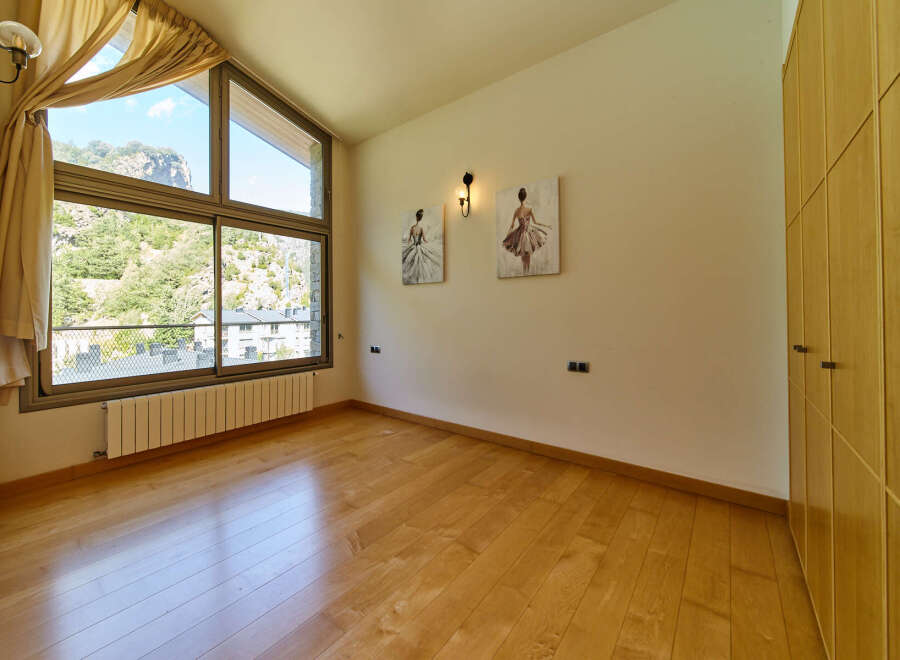 This stunning bedroom boasts a large window offering breathtaking views, complemented by hardwood floors and built-in wooden wardrobes.