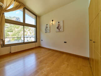 This stunning bedroom boasts a large window offering breathtaking views, complemented by hardwood floors and built-in wooden wardrobes.
