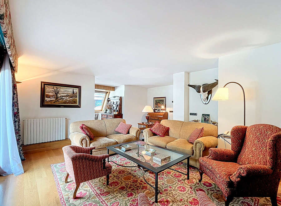 Luxurious living room with hardwood floors, featuring two beige sofas, a red armchair, and an ornate area rug.