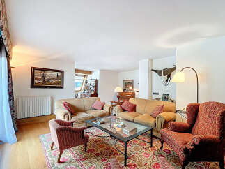 Luxurious living room with hardwood floors, featuring two beige sofas, a red armchair, and an ornate area rug.