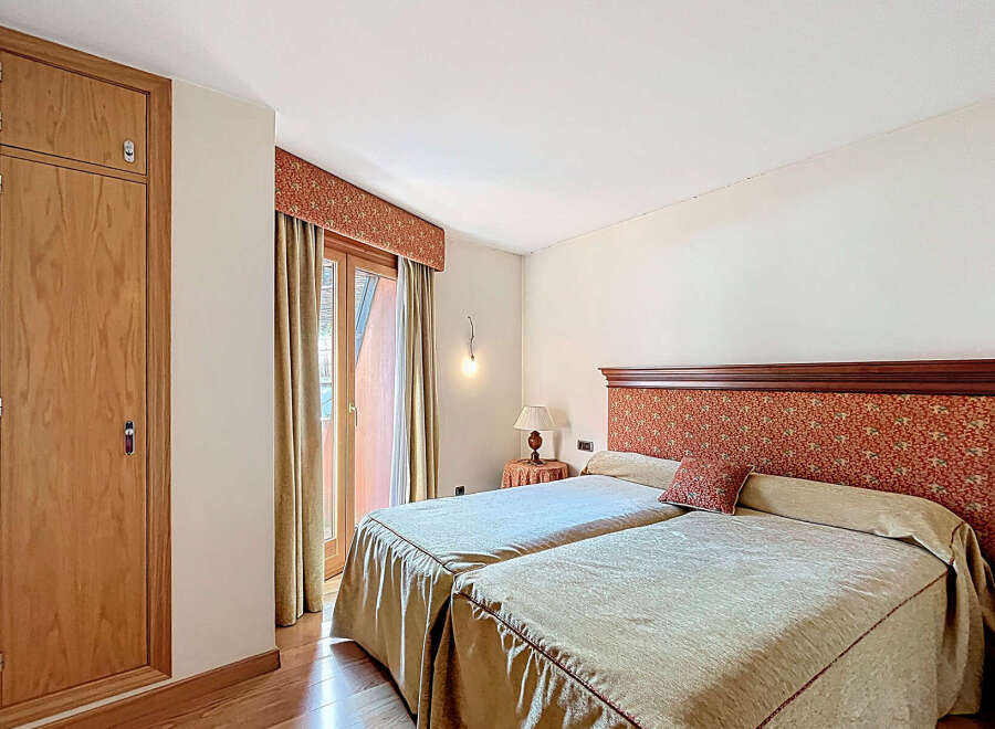 This charming bedroom boasts twin beds dressed in beige linens, complemented by a rich, patterned headboard.