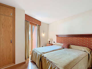 This charming bedroom boasts twin beds dressed in beige linens, complemented by a rich, patterned headboard.