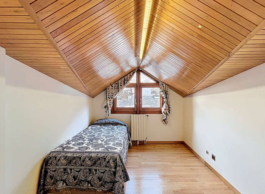 Charming attic bedroom with wood-paneled ceiling and hardwood floors.