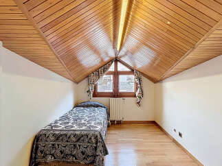 Charming attic bedroom with wood-paneled ceiling and hardwood floors.