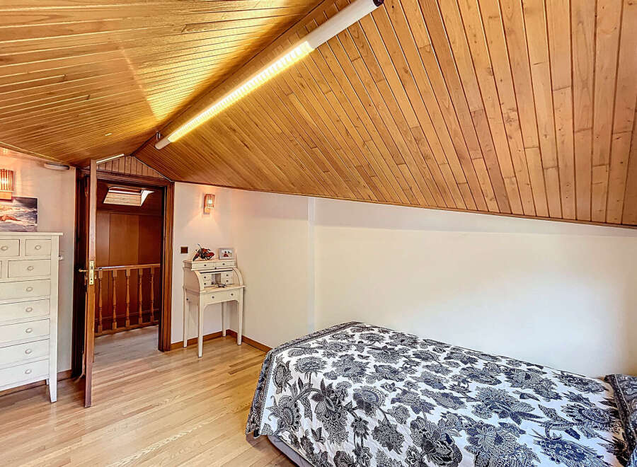 Charming attic bedroom with wood-paneled ceiling and hardwood floors.