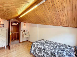 Charming attic bedroom with wood-paneled ceiling and hardwood floors.