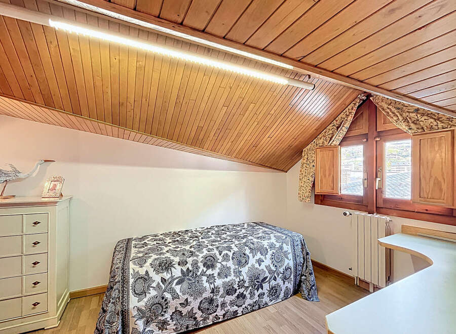 Charming attic bedroom with wood-paneled ceiling and sloped walls.