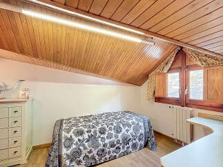 Charming attic bedroom with wood-paneled ceiling and sloped walls.