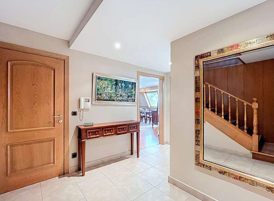 Elegant entrance hall with hardwood floors, a wooden console table, and a large ornate mirror reflecting a staircase.