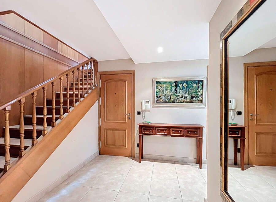 Elegant entrance hall with a stunning wooden staircase, complemented by a tasteful console table and a large mirror reflecting the hallway's beauty.
