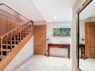 Elegant entrance hall with a stunning wooden staircase, complemented by a tasteful console table and a large mirror reflecting the hallway's beauty.