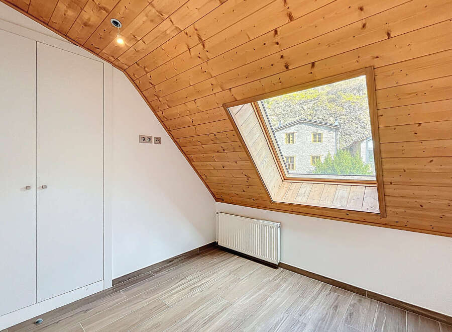 This charming attic room features a unique sloped ceiling with warm wooden paneling, creating a cozy and inviting atmosphere.